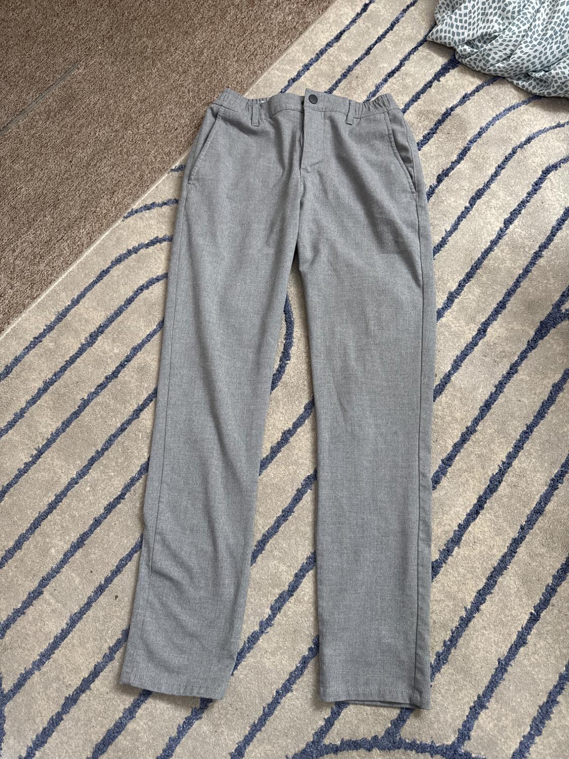 Light grey trousers with an elasticated waist, laid out on a rug with wavy blue stripes. Casual and relaxed composition.