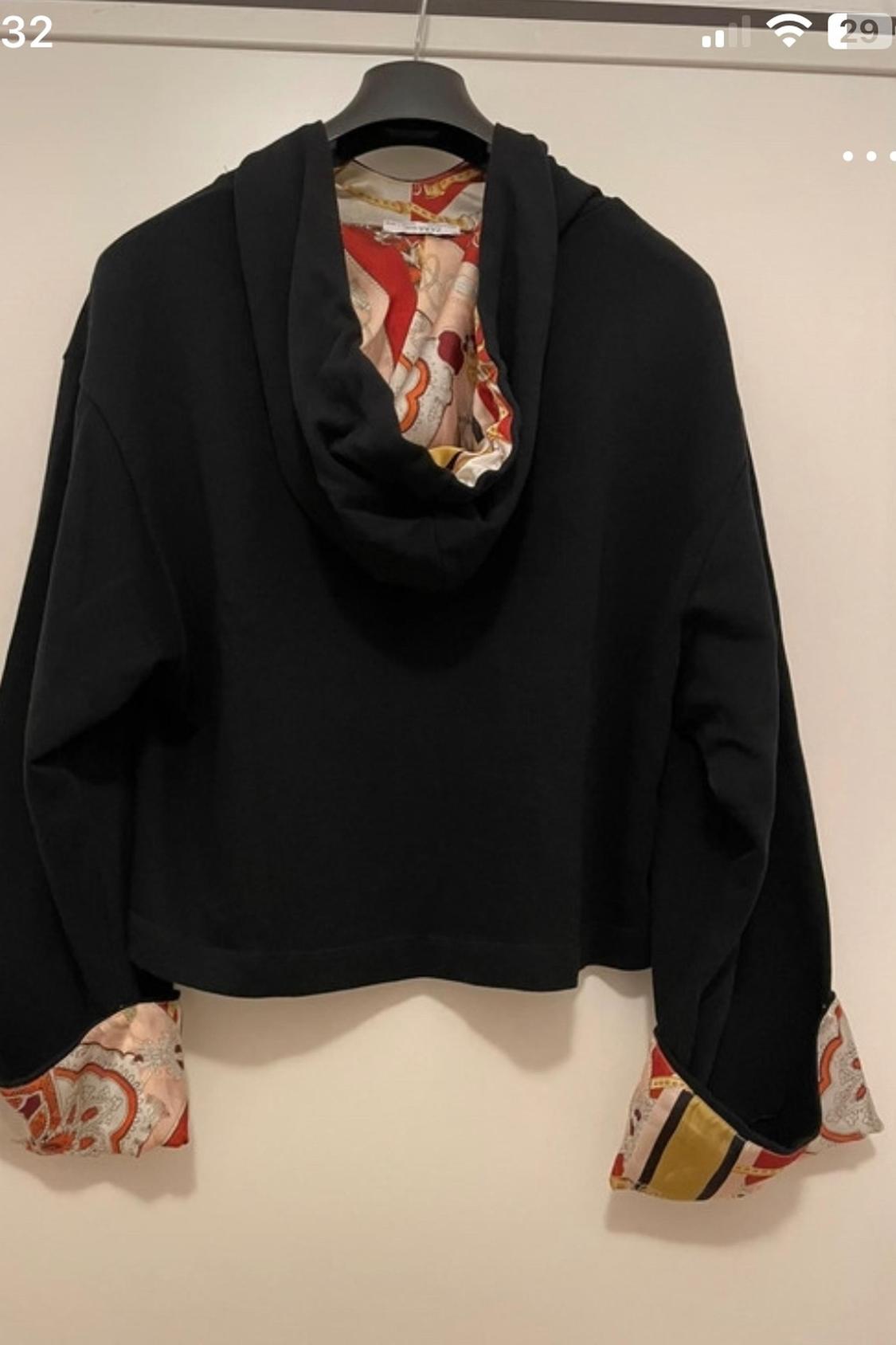 Rear view of a black hoodie with colourful print details on the inside and the cuffs.