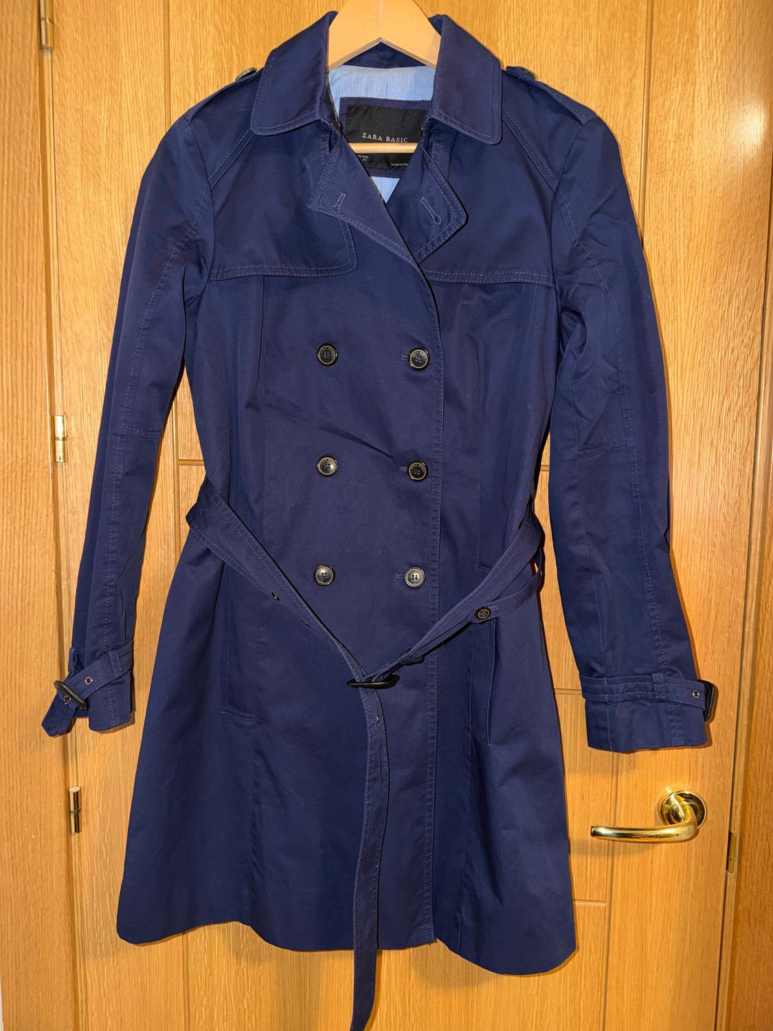 Navy blue double-breasted coat hanging on a wooden door. Visible label: "ZARA BASIC".