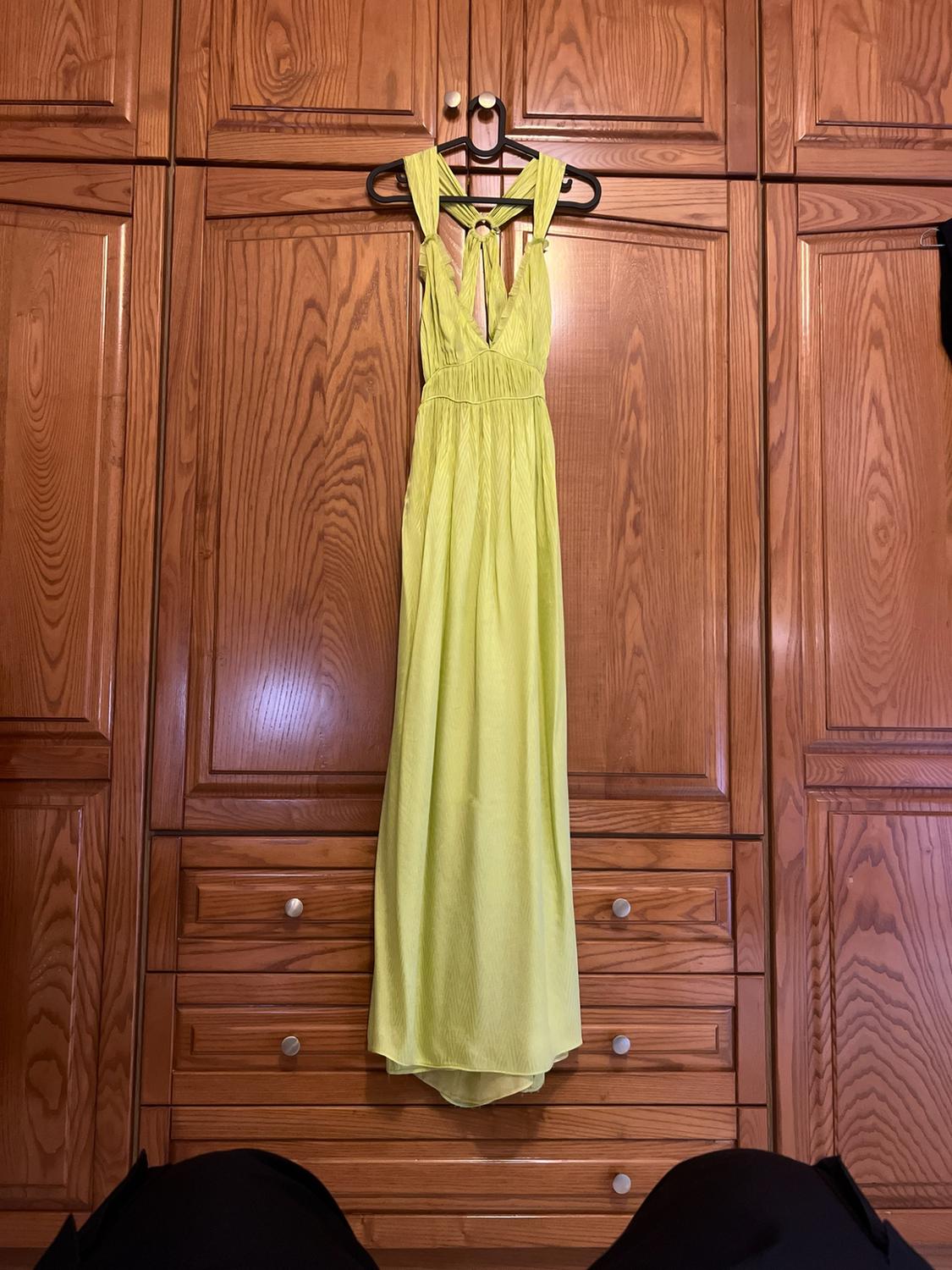 Lime green flowing maxi dress with a V-neck, hanging on a black hanger on the doors of a classic wooden wardrobe.