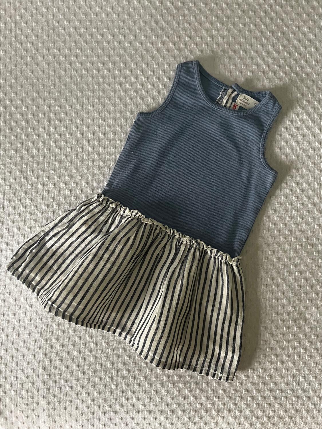 Front view of a blue sleeveless dress with a black and white striped skirt.