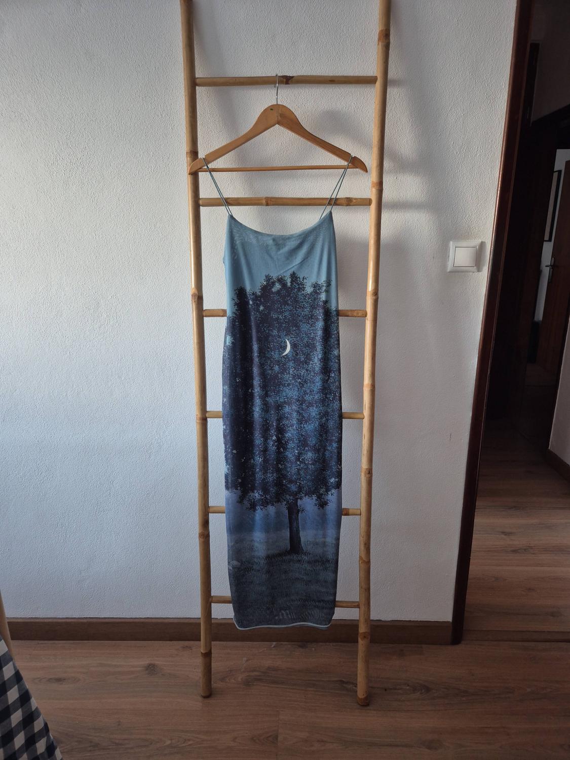 Long strappy dress with a night-time tree and moon print, hanging on a wooden ladder leaning against a white wall.
