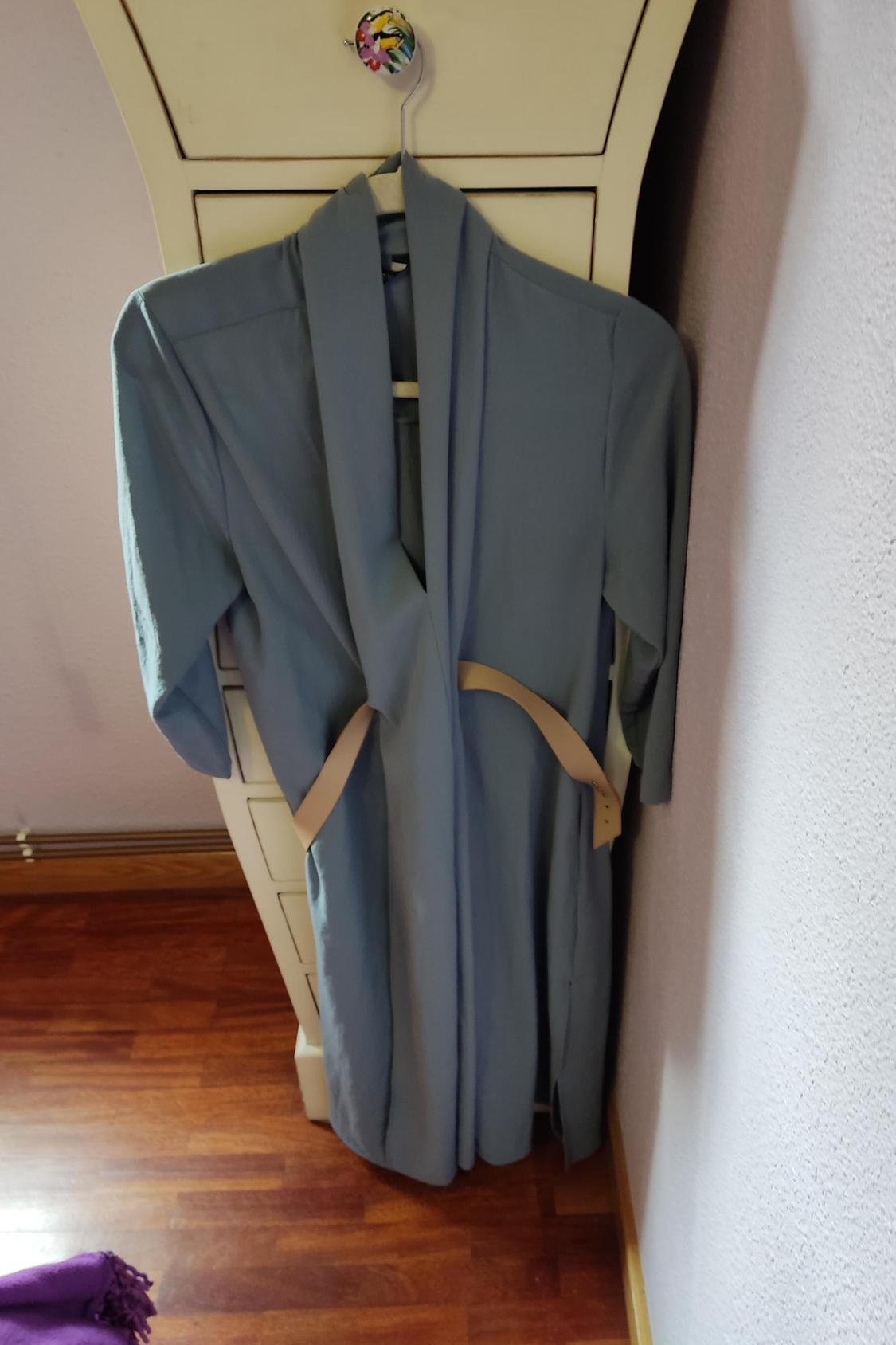 Front view of a blue dressing gown with a beige belt, hanging on a hanger.