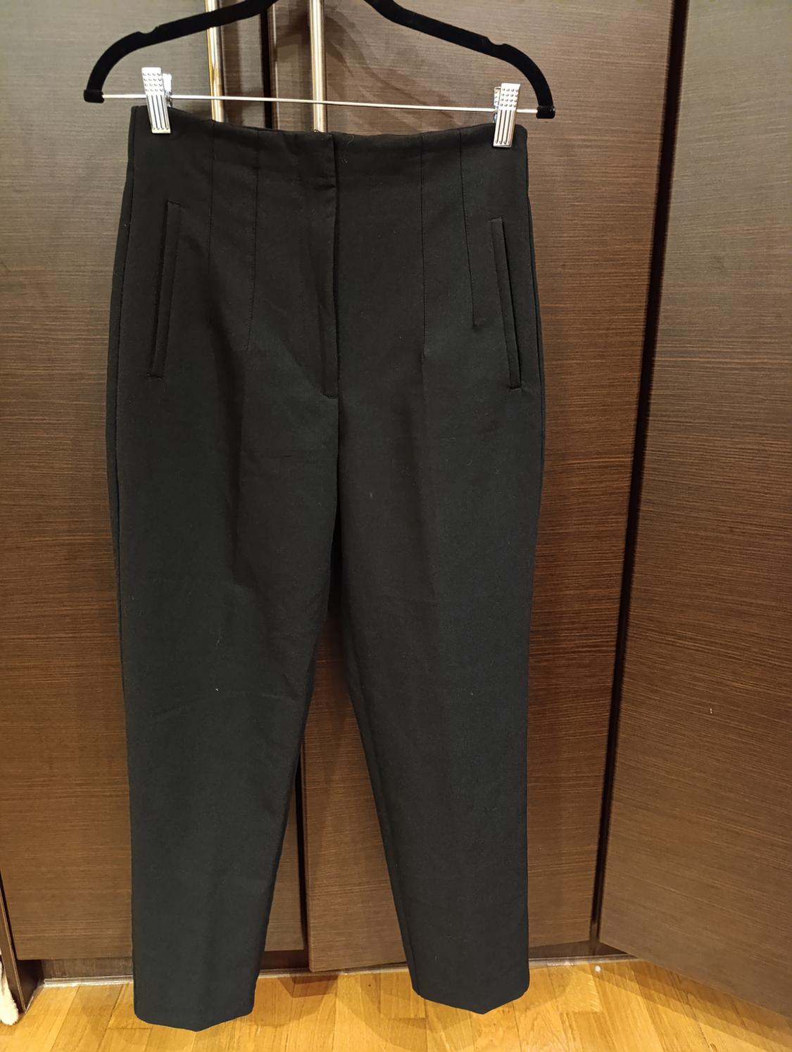 Black trousers hanging on a hanger against a brown wooden background.