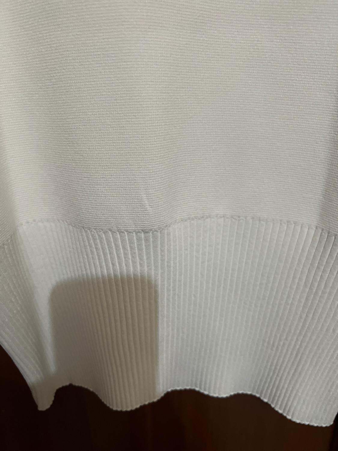 Detail of a white knitted garment with a fine texture at the top and a ribbed hem.