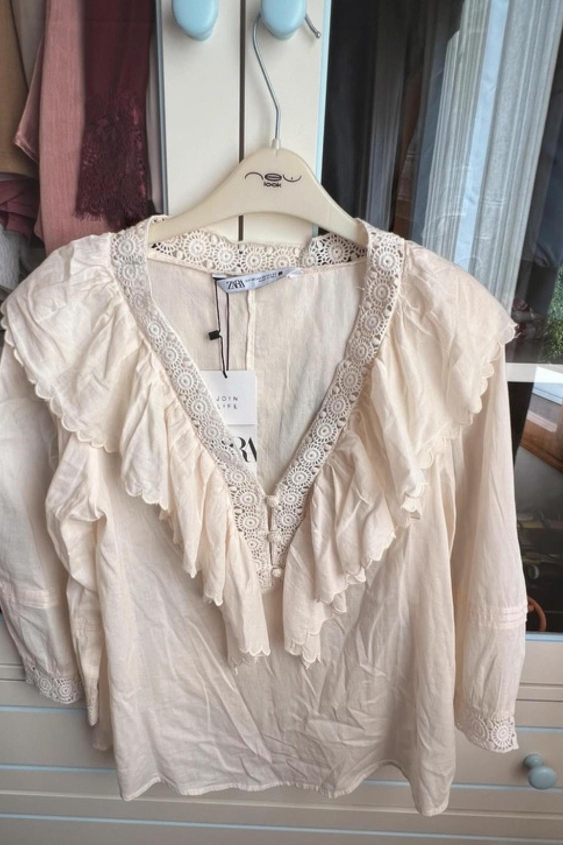 Front view of a beige blouse with ruffles and lace on the V-neck.