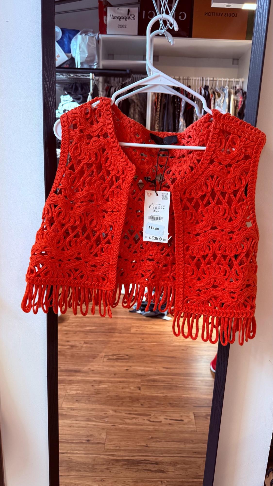 Red open-knit fringed vest hanging in front of a mirror reflecting a wardrobe. Text: $59.90, S 26, asos, LOUIS VUITTON.