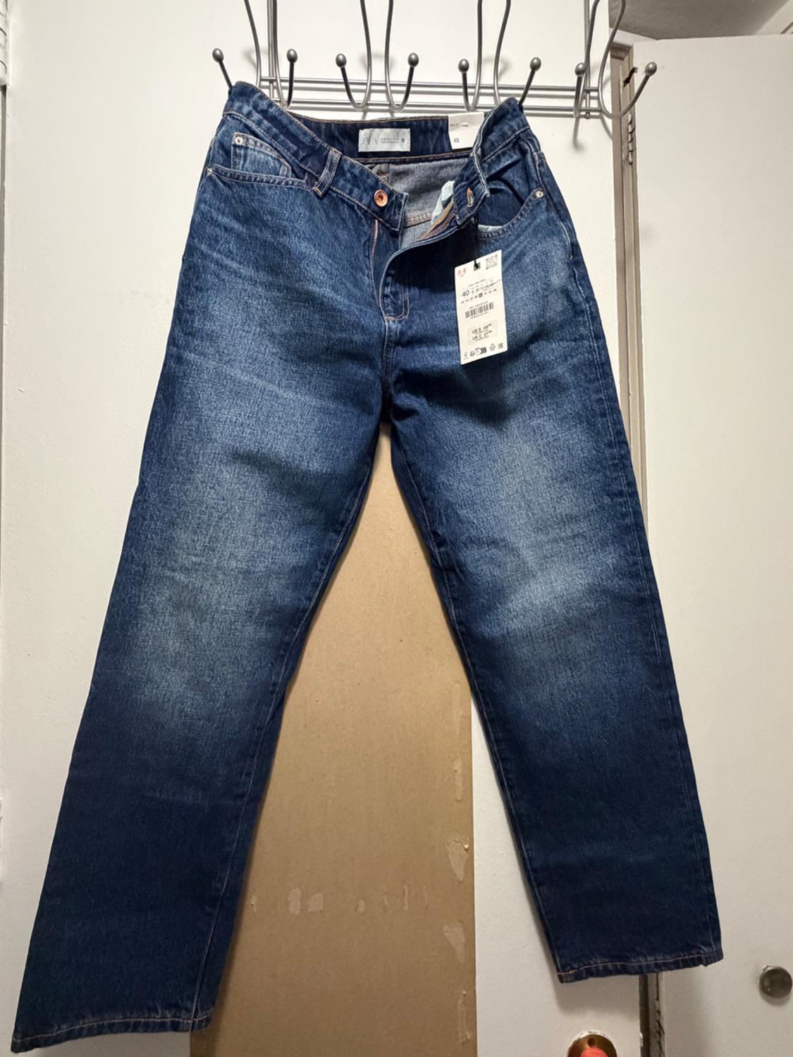 Blue denim pants hanging on a metal rack above a white door, with a washed effect and a visible label at the waist.