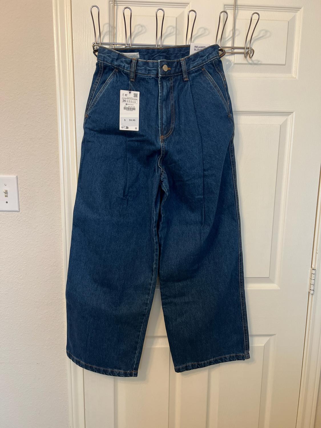Wide-leg blue jeans hanging on a white door. Visible labels bearing the text RELAXED SLOUCHY, 36 and $59.90.