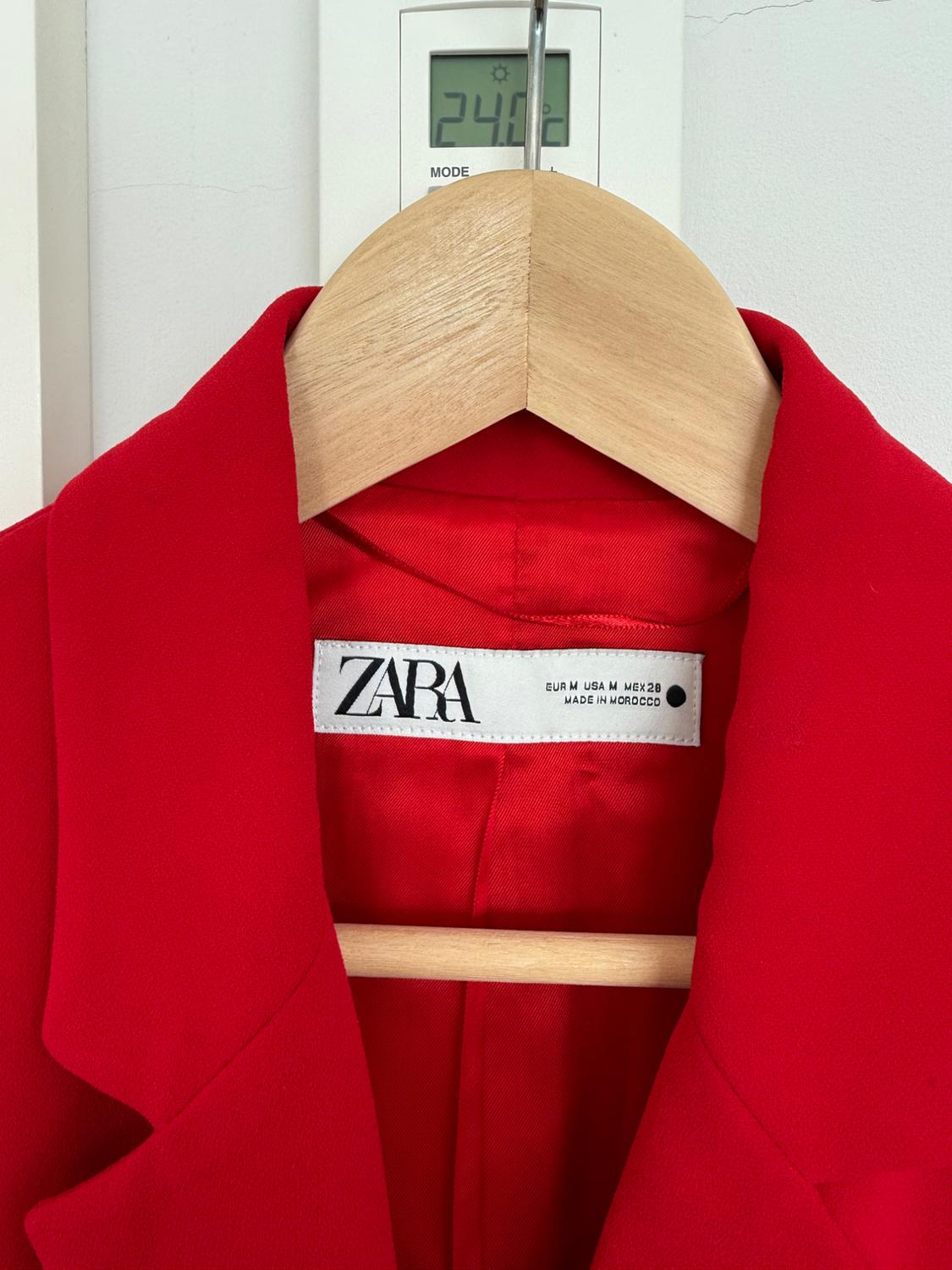 Red Zara jacket on a wooden hanger, label visible. Background with thermostat displaying 24.0°C.