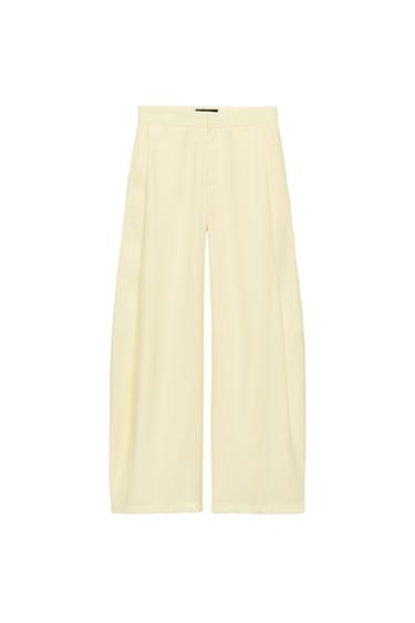Front view of wide-leg beige trousers with side pockets and pleats on the front.