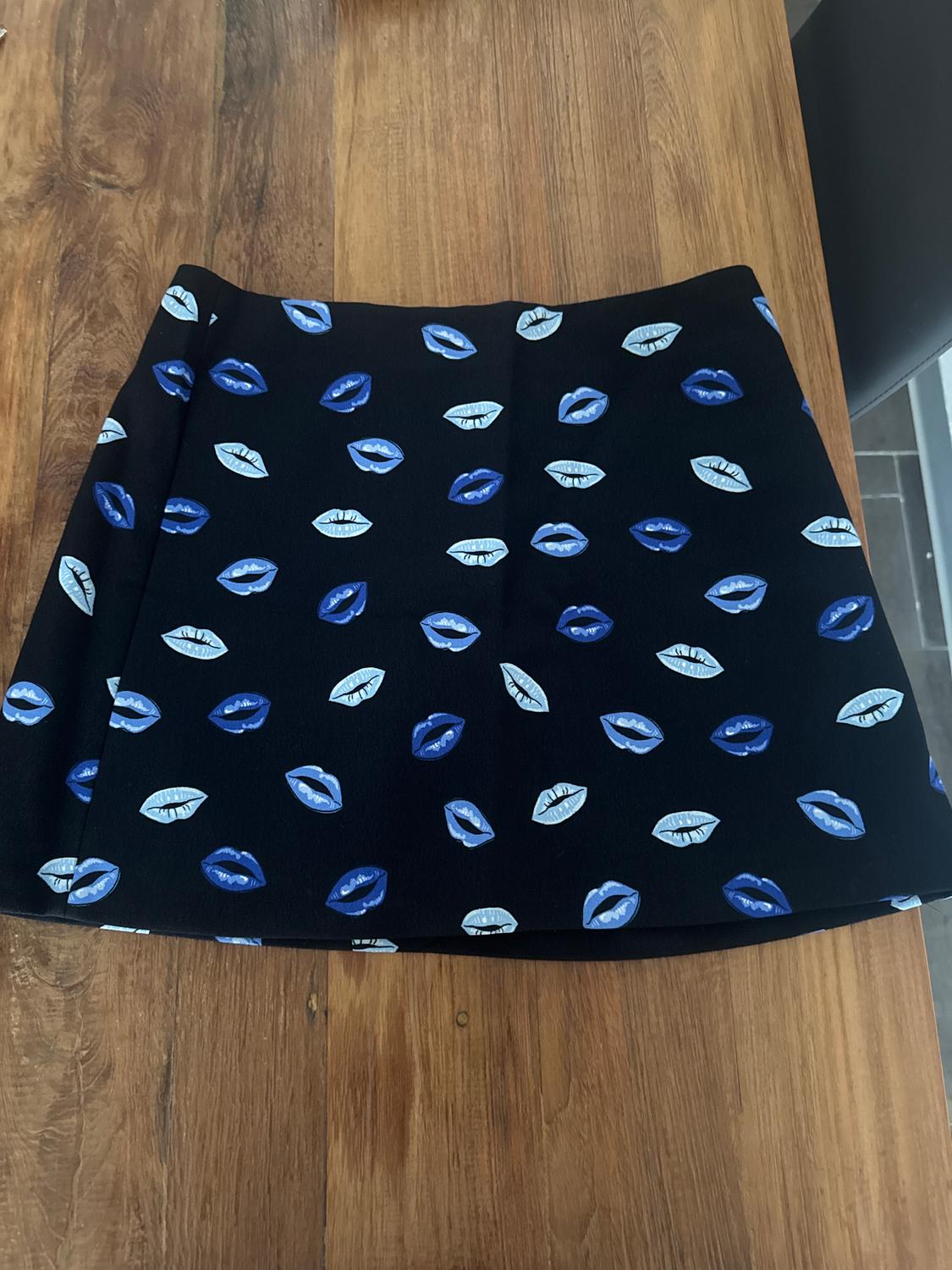 A black skirt with a blue and white lip design is on a wooden table.