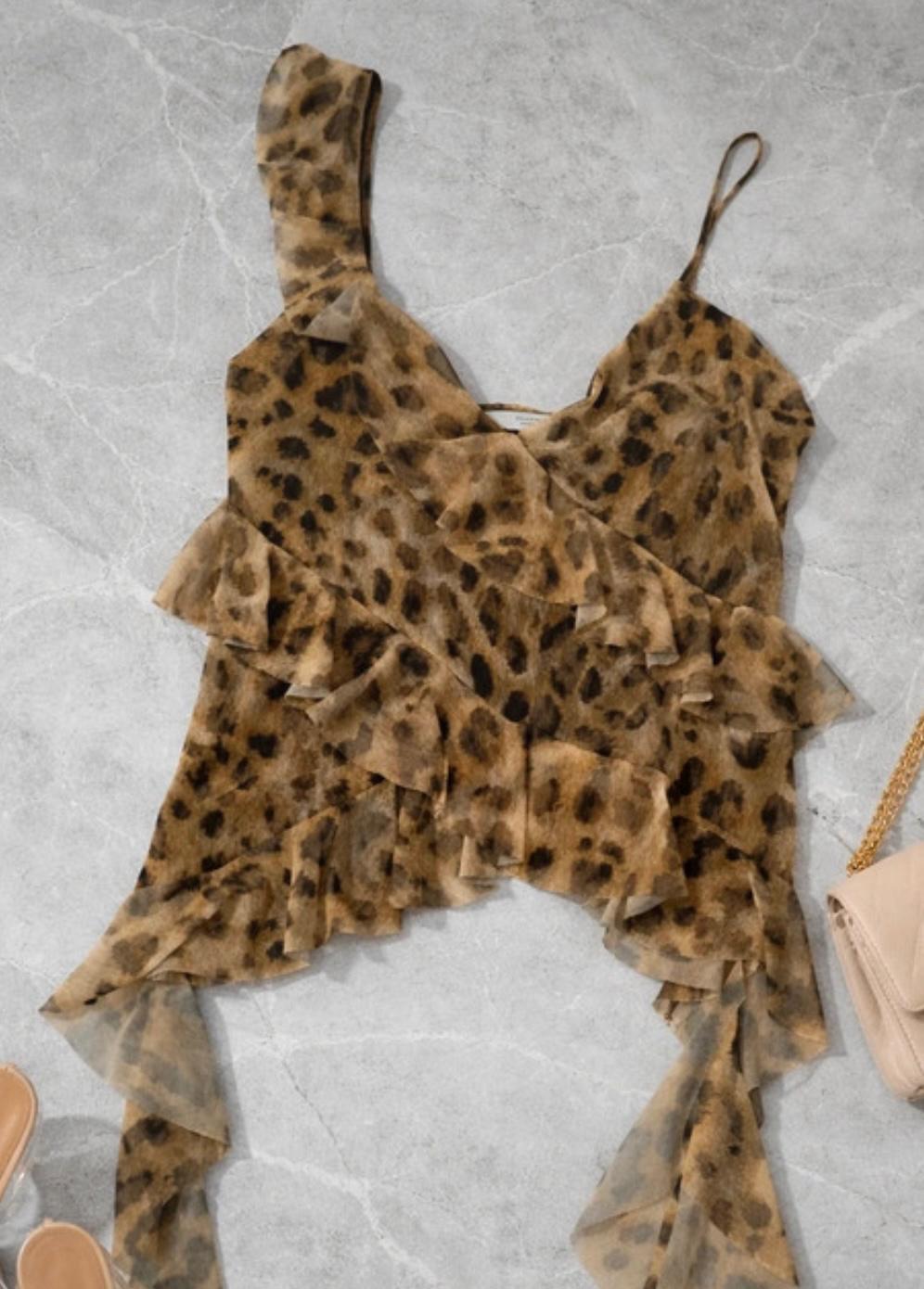 Animal print camisole with ruffles on a grey background. To the right, a beige bag with a gold chain.