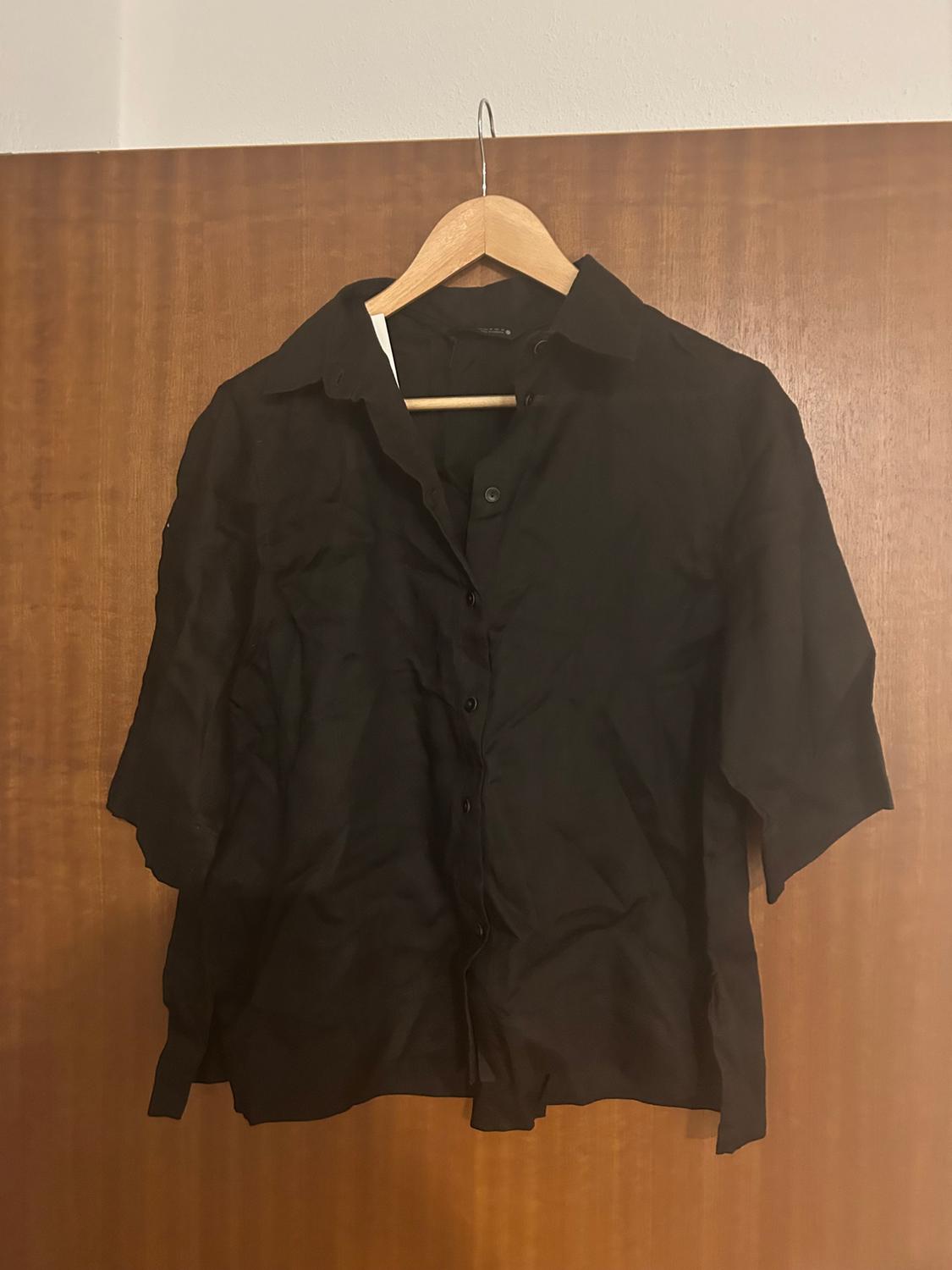 Black short-sleeved shirt hanging on a wooden hanger against a brown wooden background.