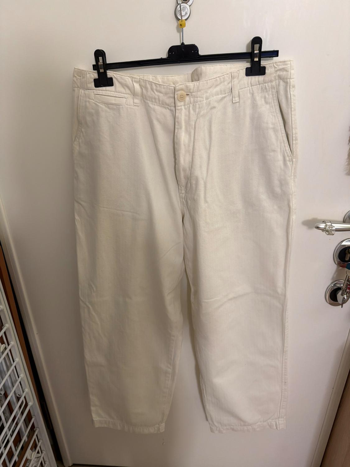 White trousers hanging on a black hanger over a white door. The hanger is held by a metal hook.