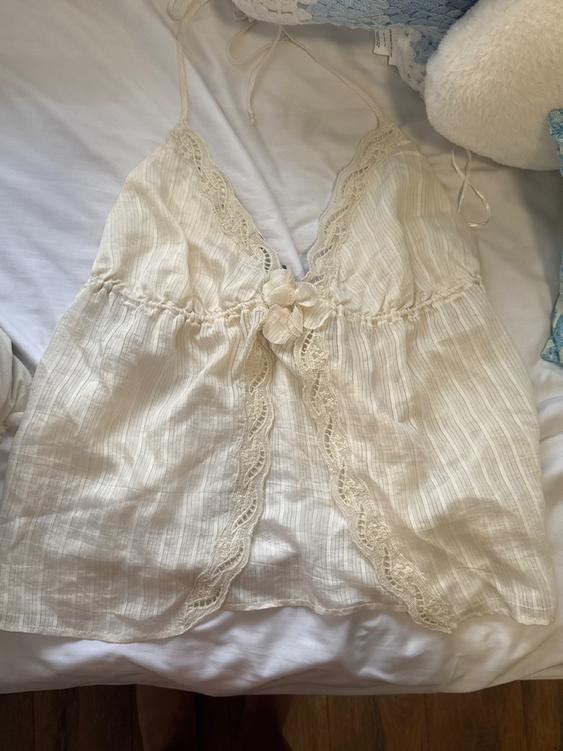 White camisole with lace and a floral detail in the center, on a bed with white and blue pillows.