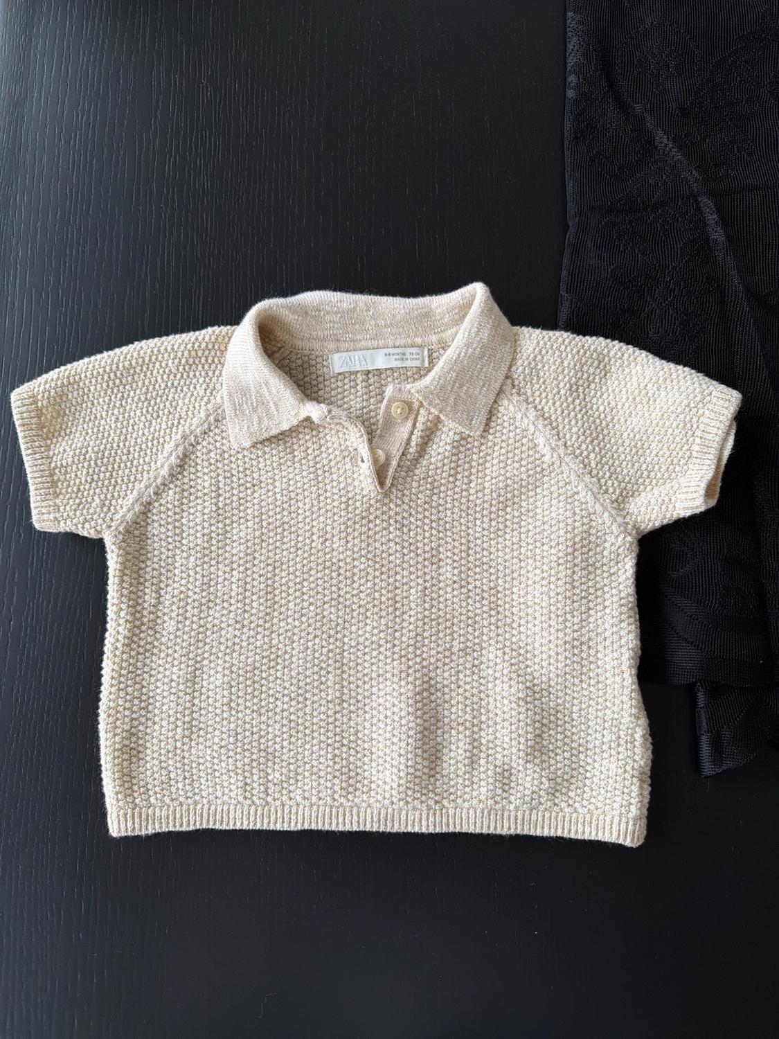 Beige pointelle short-sleeve polo on a dark background next to a black fabric. Text: zara 6-9 MONTHS 74 CM MADE IN CHINA.