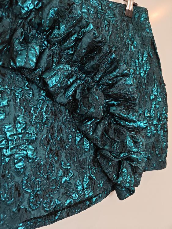 Blue shiny fabric mini skirt with a crinkled texture and ruffles, hanging on a hanger against a white background.