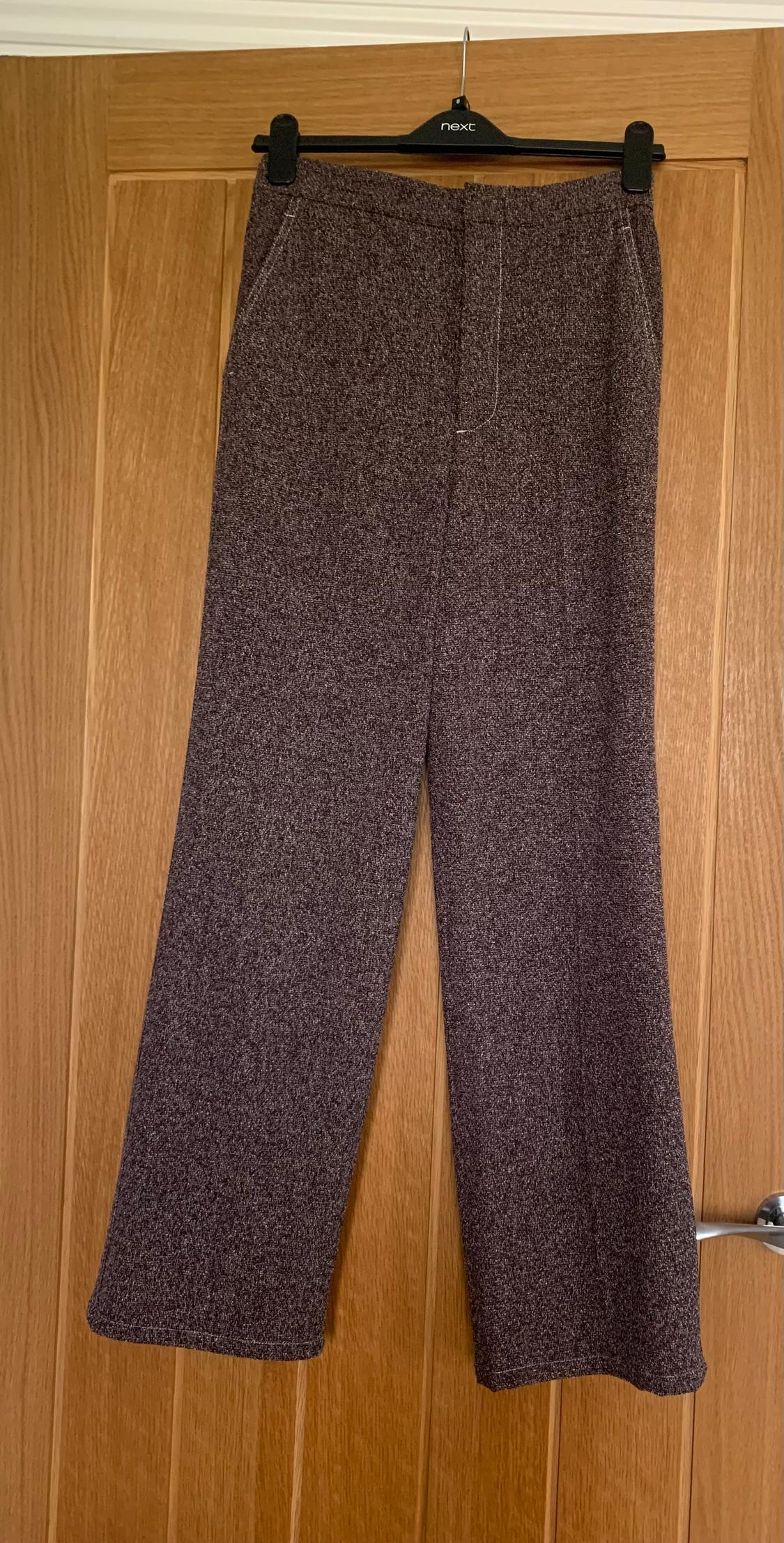 Grey trousers hanging on a black "next" branded hanger, over a light wooden door.