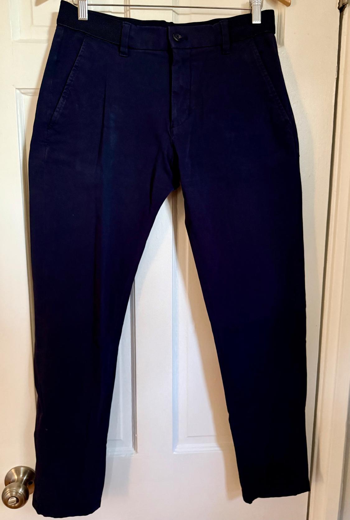 Dark navy blue pants hanging from a hanger over a white door.