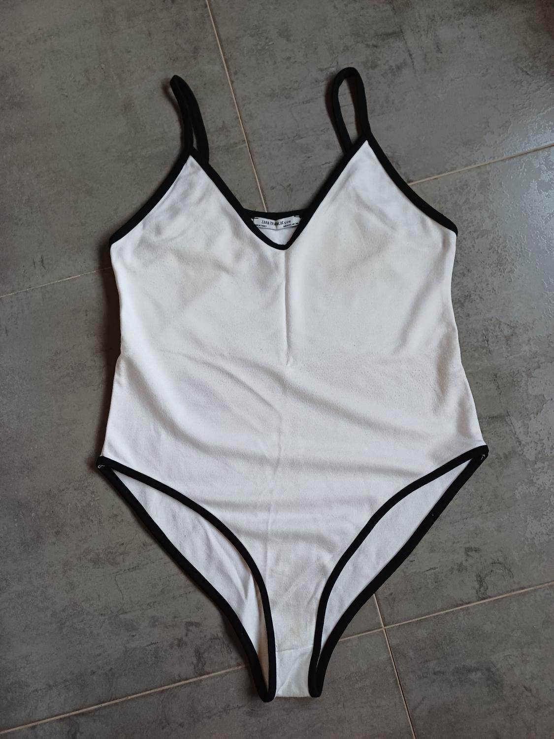 White bodysuit with black trim and straps on a grey tiled floor. Label with the text ZARA TRAFALUC.
