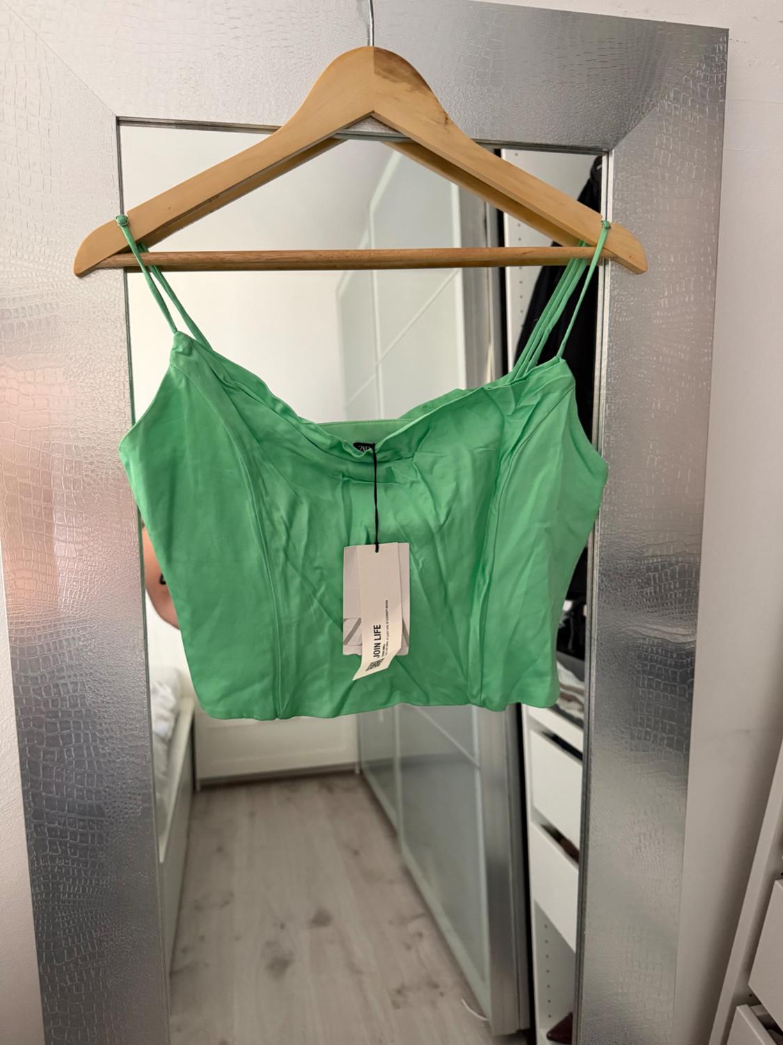 Green camisole top hanging on a wooden hanger in front of a mirror. Visible "JOIN LIFE" tag.