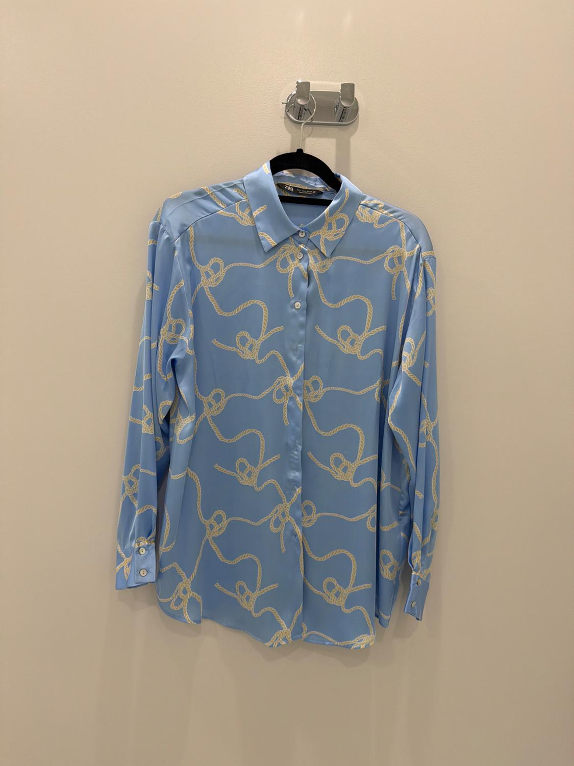 Light blue button-down shirt with a white rope pattern, hanging on a black hanger against a light-colored wall.