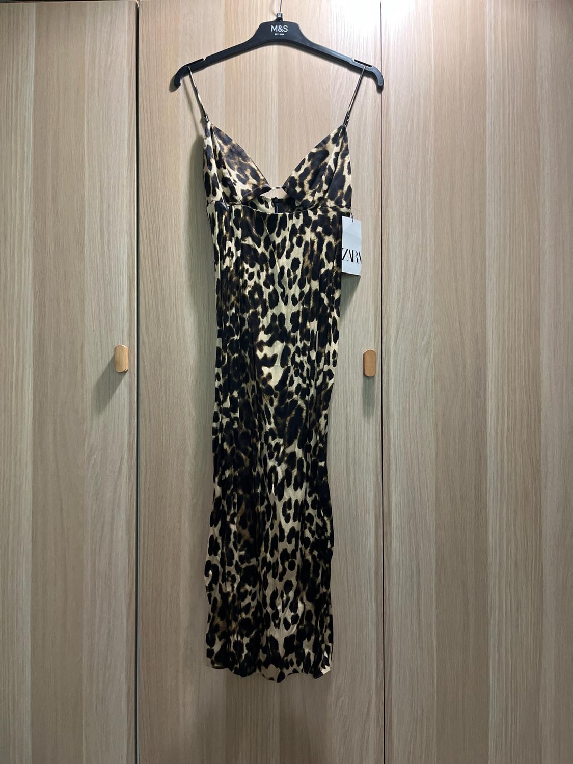 Leopard print slip dress hanging in a light-coloured wooden wardrobe. Text: M&S on the hanger and ZARA on the label.