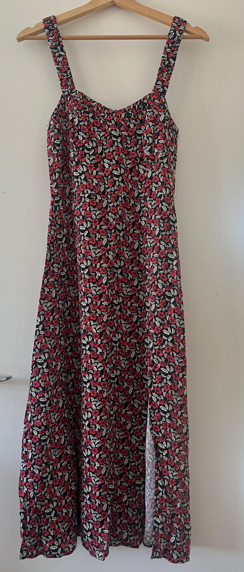 Black strappy dress with a red floral and white leaf print, hanging on a wooden hanger against a white door. It has a side slit.
