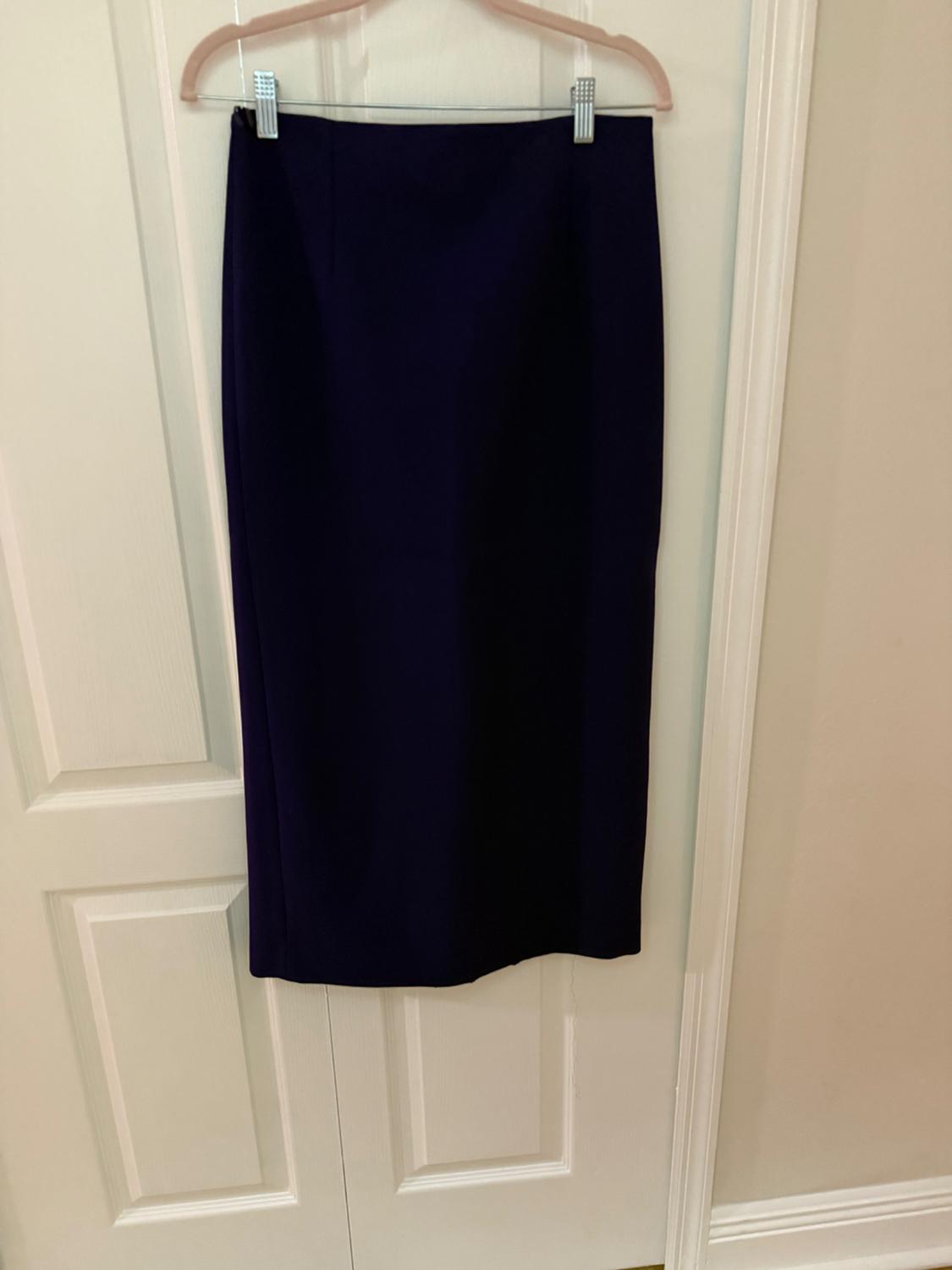 Dark-colored long skirt hanging on a hanger over a white door. Simple and minimalist atmosphere.