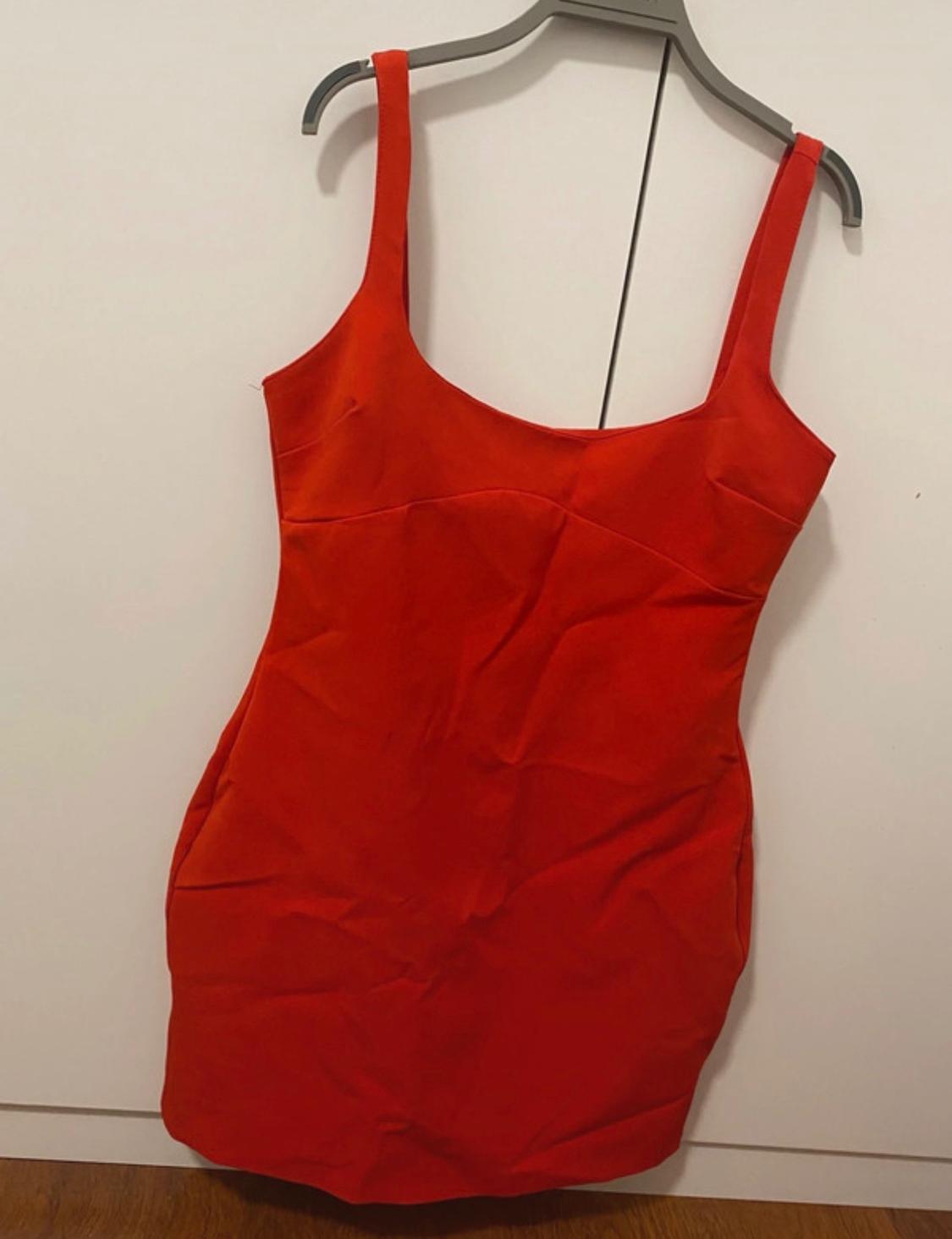 Red, tight-fitting, strappy mini dress hanging on a grey hanger in front of a white wardrobe.