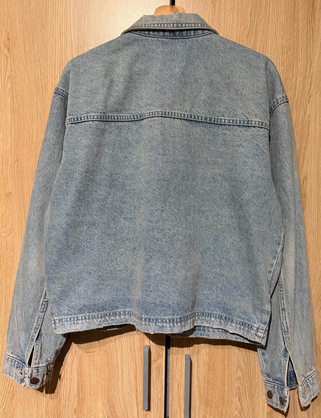 Light blue denim jacket hanging on a wooden hanger, viewed from behind, against a light wooden background.