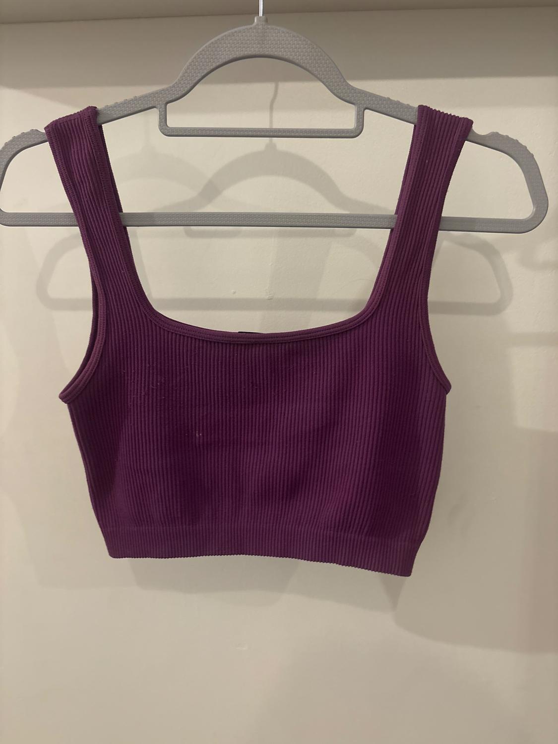 Purple ribbed knitted crop top with wide straps, hanging on a grey hanger against a white background.