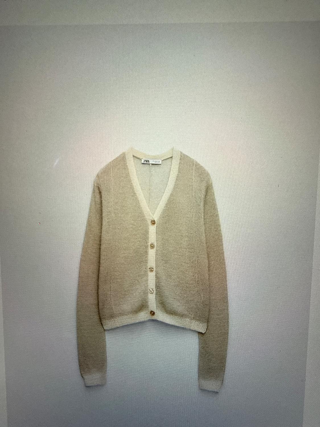 Beige knit cardigan with a V-neck, button closure, and light trim against a neutral background. ZARA label visible on the collar.