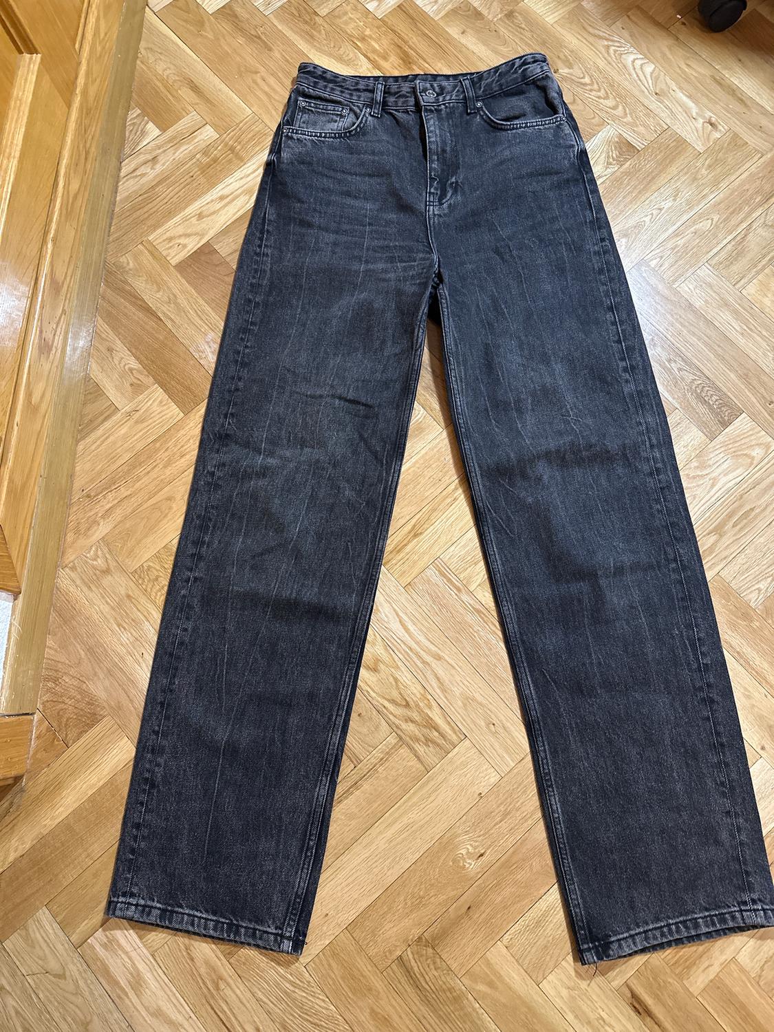 Black straight-leg jeans laid flat on a light-coloured herringbone wood floor.
