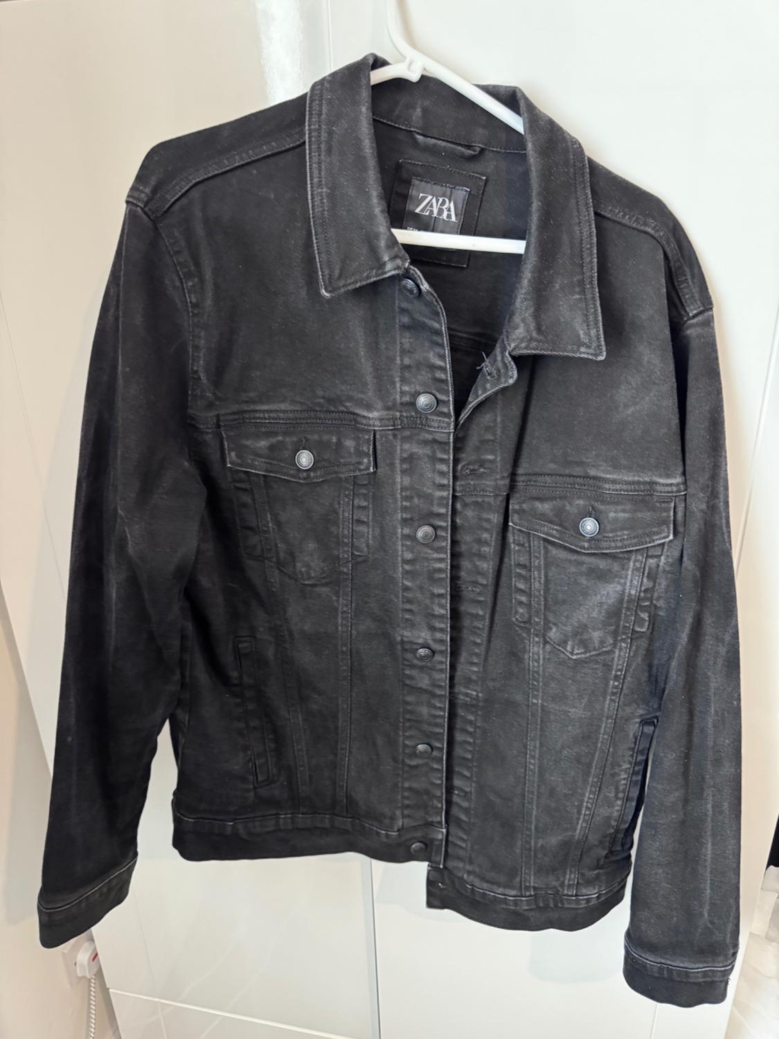 Black denim jacket hanging on a white hanger, with a visible Zara label inside the collar.