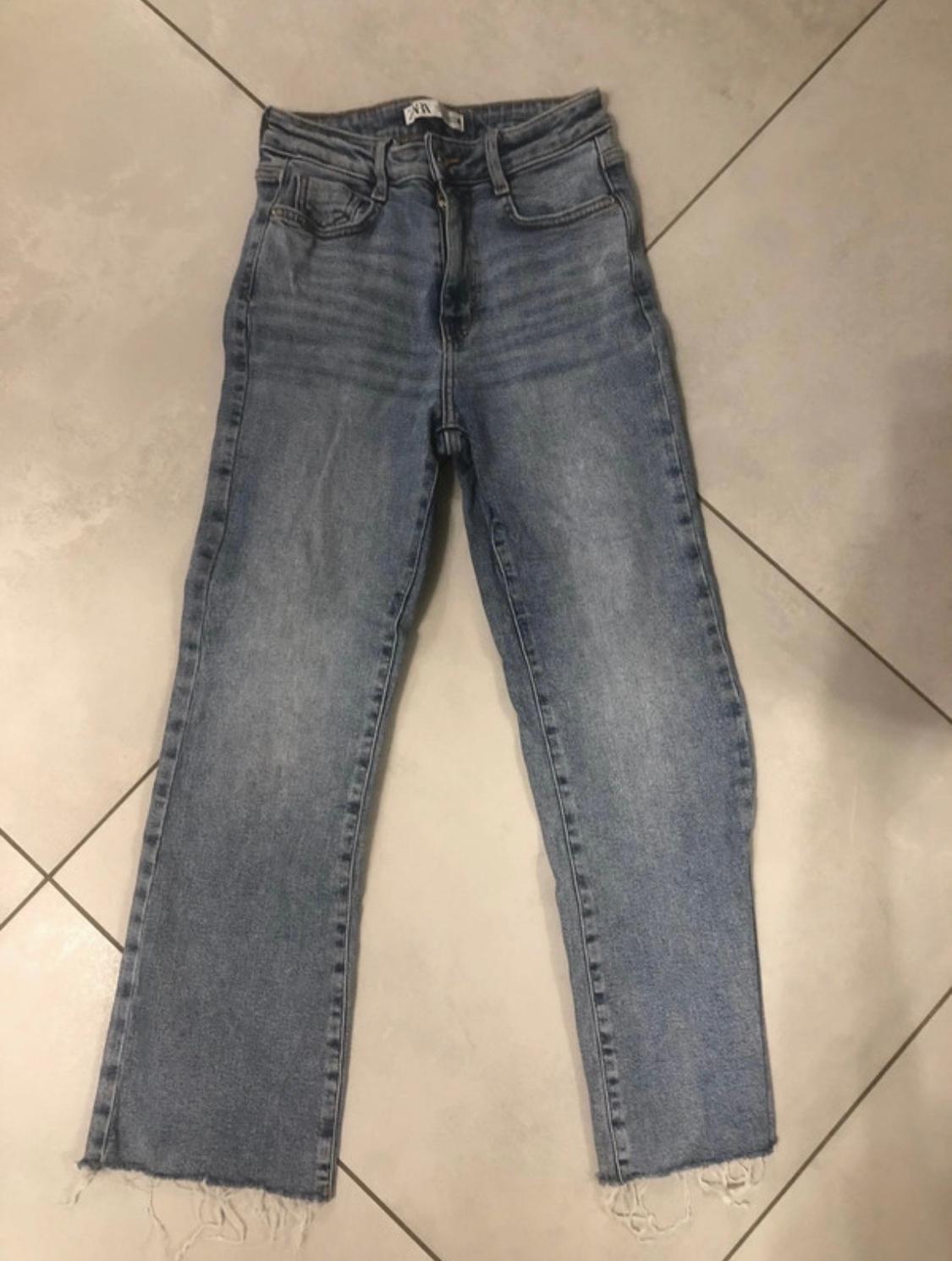 Light blue high-waisted jeans with a frayed hem on a tiled floor. The label reads ZARA.