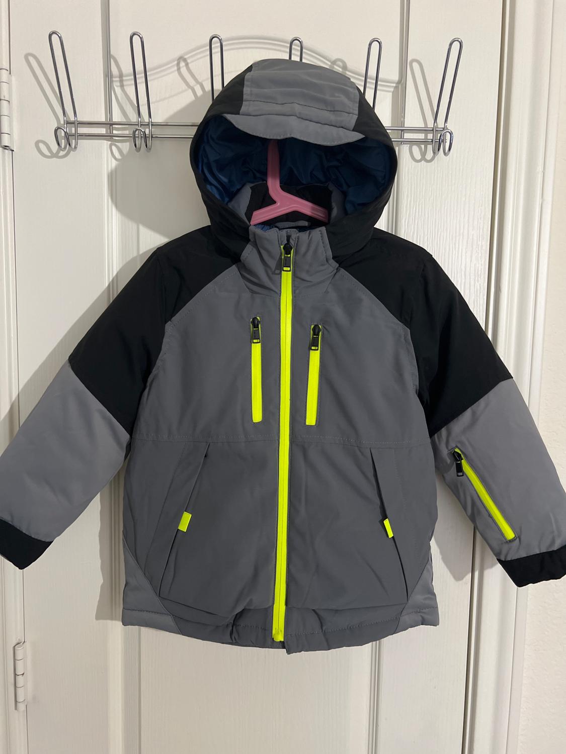 Gray and black coat with a hood and neon yellow zippers, on a pink hanger hanging from a metal coat rack over a white door.