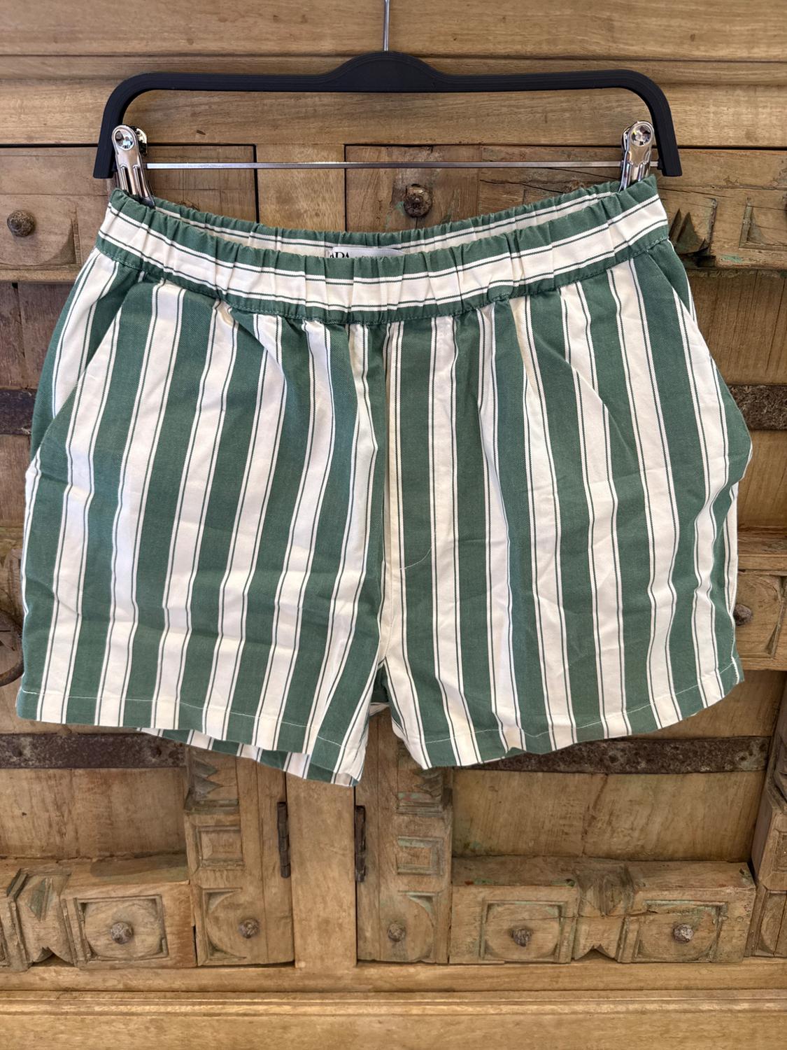 Green and white striped shorts hanging on a black hanger against a background of carved wood.