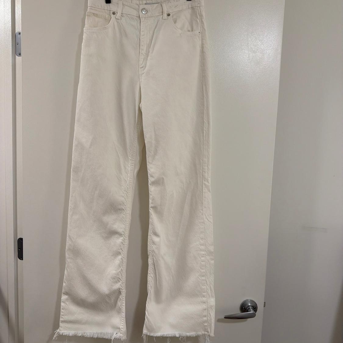 Cream-coloured straight-leg jeans with a frayed hem, hanging on a white door.