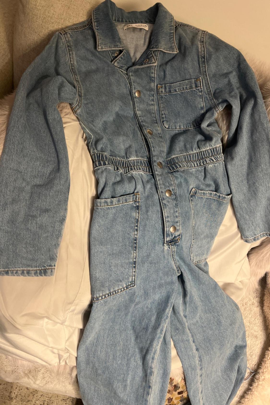 Front view of light blue denim dungarees with front pockets and metal buttons.