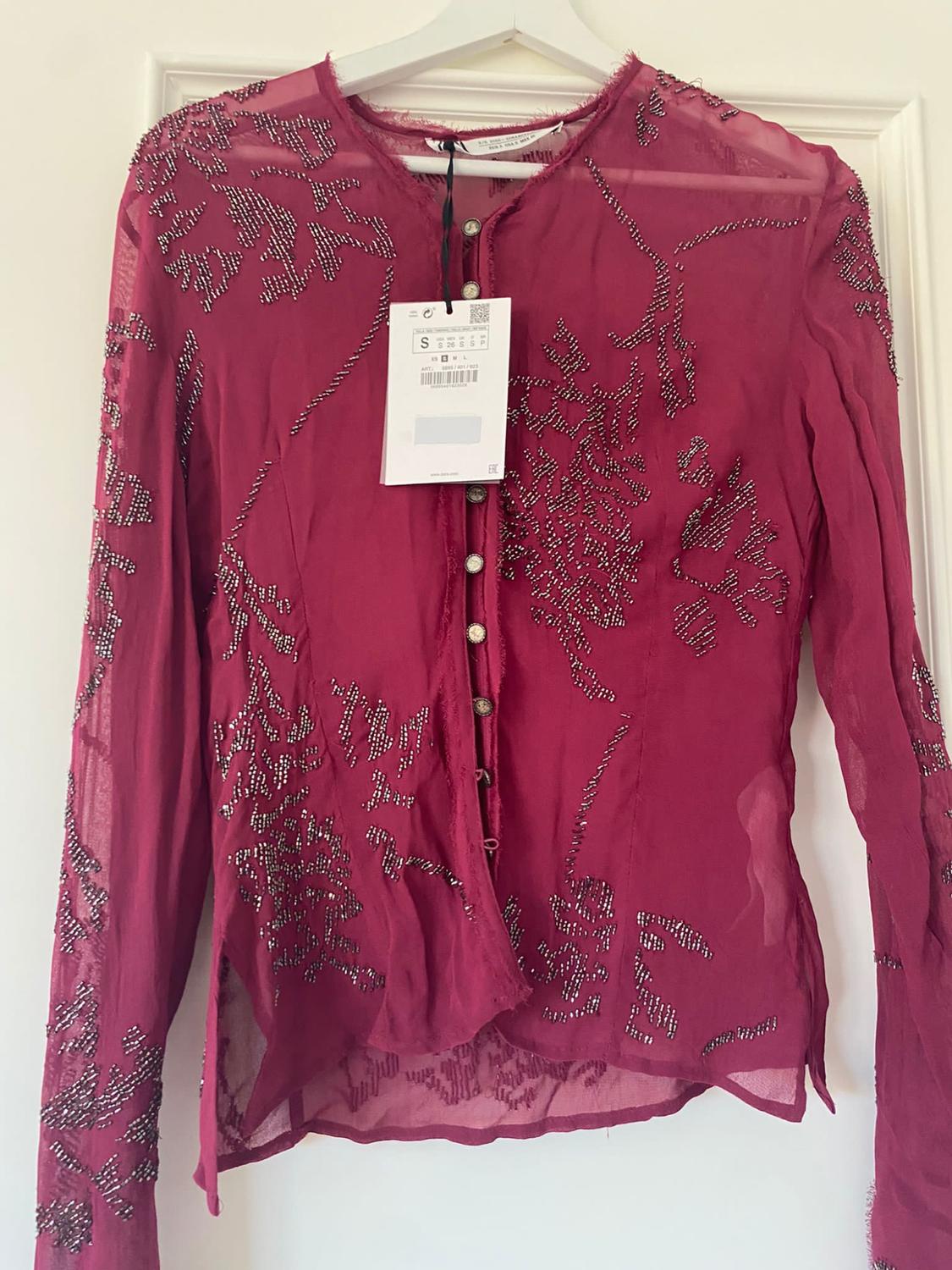 Red sheer blouse with silver bead embroidery, hanging on a white hanger. Visible label with size S.