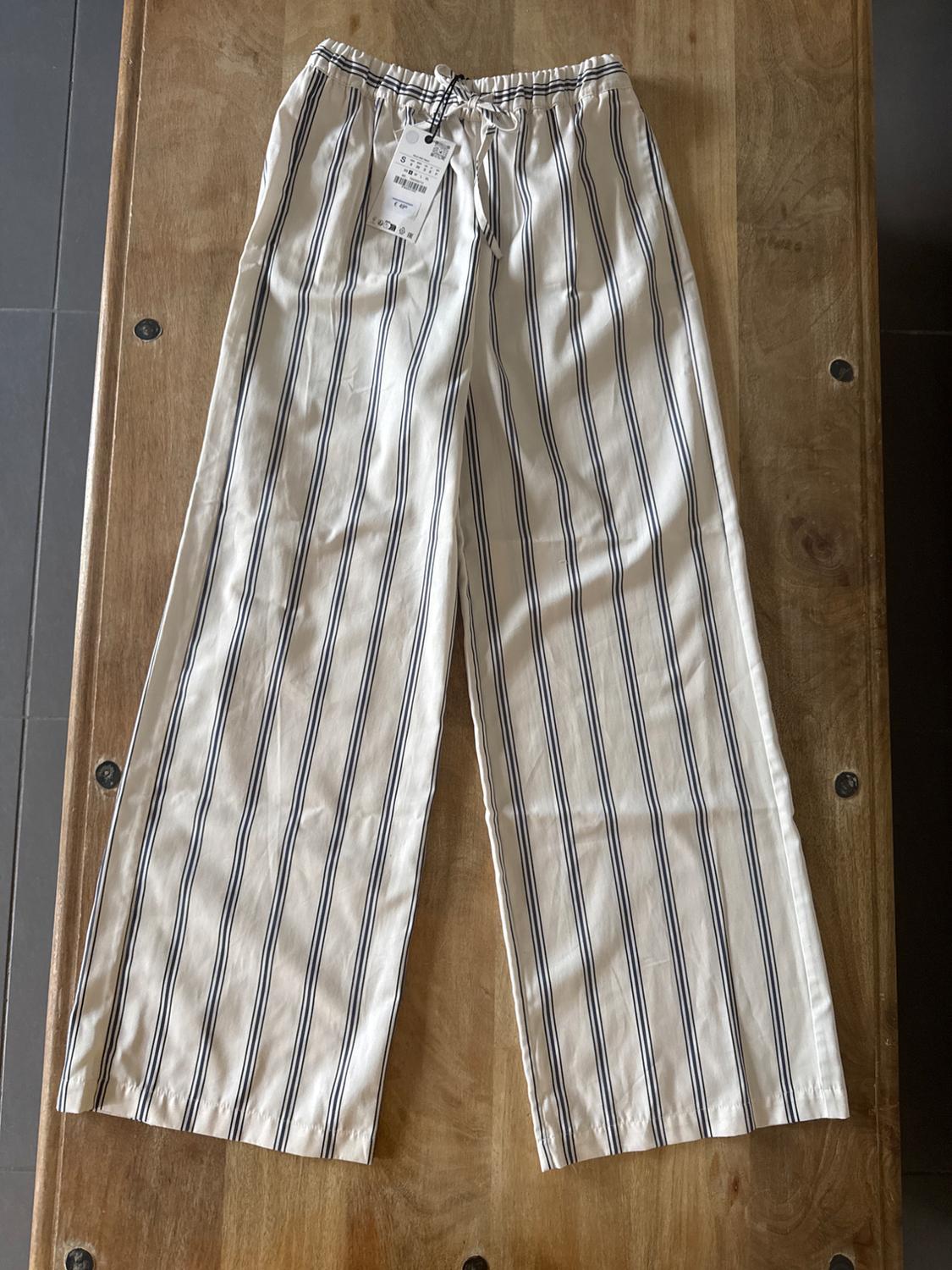 Black and white vertical striped trousers on a wooden table. Hang tag visible at the waist.