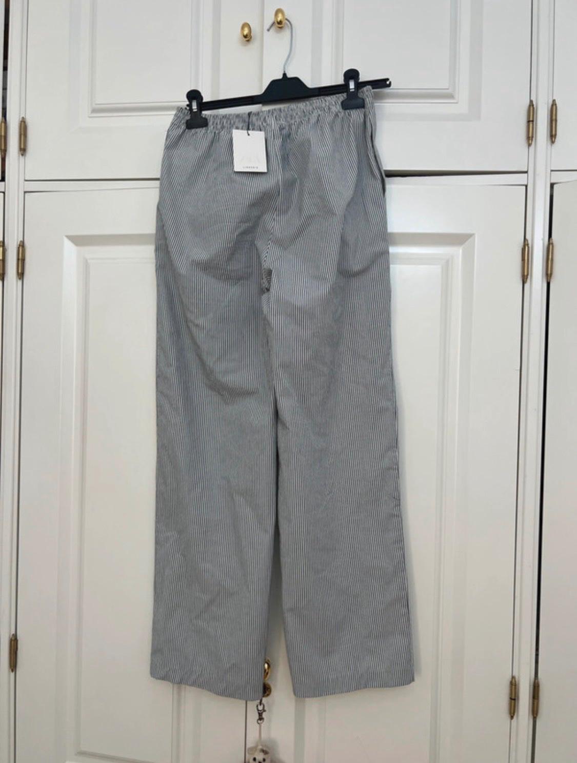 Pinstriped flowing trousers with an elasticated waist hanging on a hanger in a white wardrobe. Label with ZARA text.