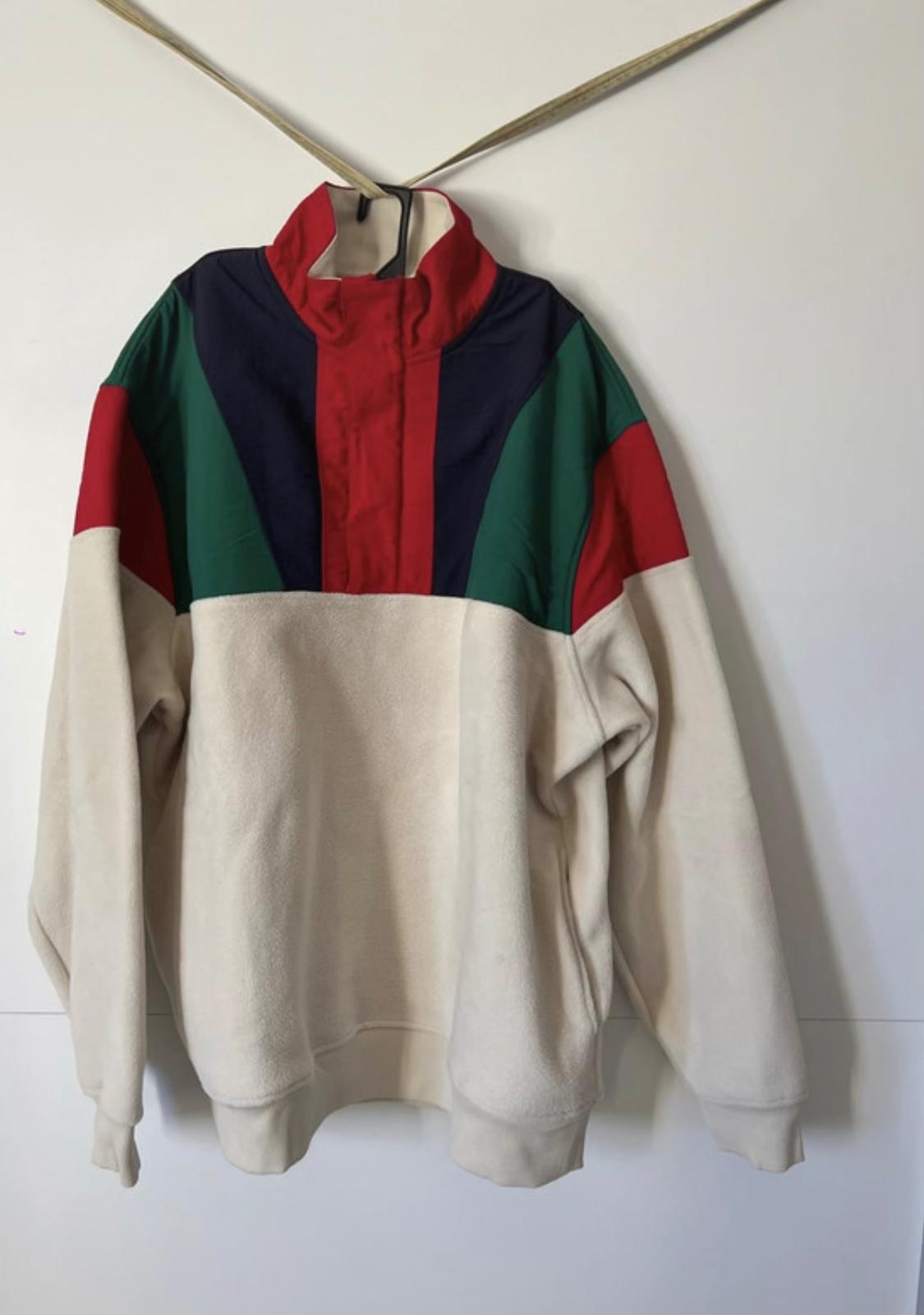 Hoodie hanging with cream, blue, red and green design on the top. White background.