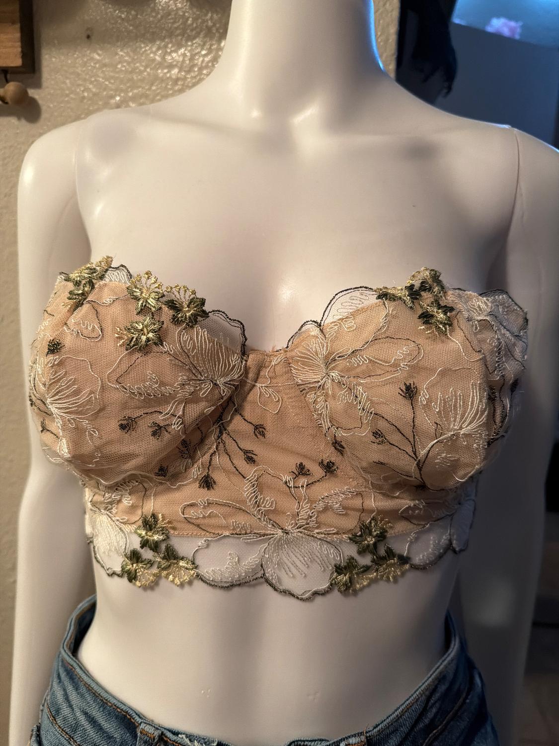 Mannequin with a beige and green floral lace top, embroidered details, paired with blue jeans. Indoor room background.