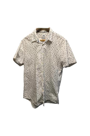 Short-sleeved white shirt with a star print on a wooden hanger against a white background. ZARA text on the label.