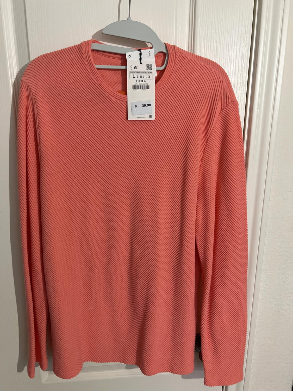 Coral long-sleeved sweater with ribbed texture, hanging on a white hanger. Visible tag with price of $39.90.