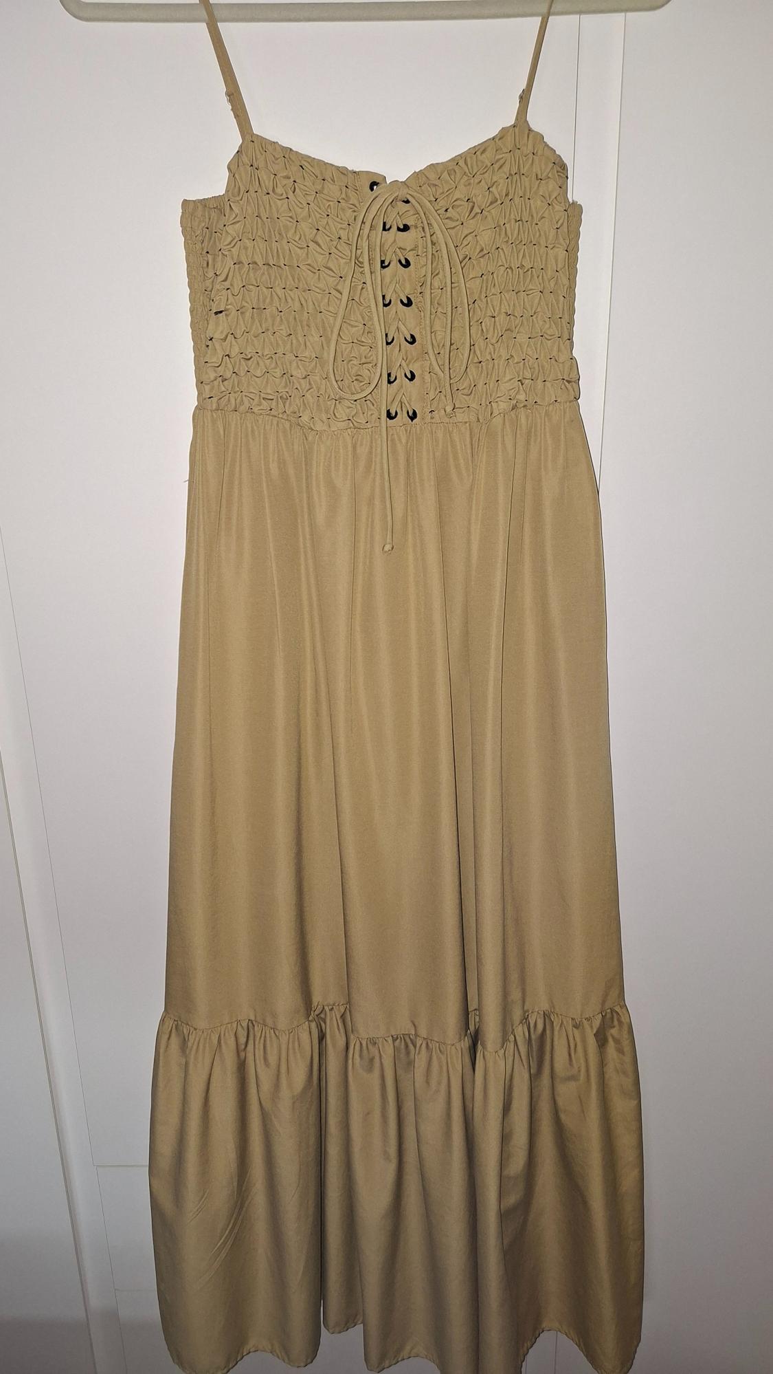 Beige dress with thin straps, ruched top and lace-up detail on the chest. Full skirt with ruffles.