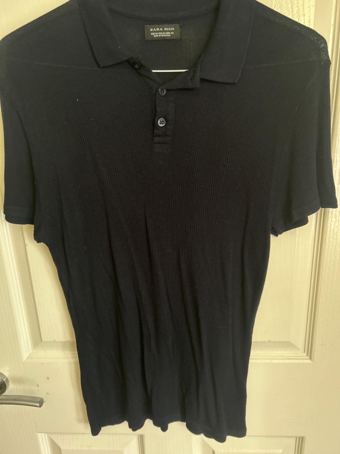 Front view of a black polo shirt with a collar and a three-button placket.